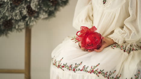 Girl-in-a-Christmas-holiday-festive-dress-holding-a-red-ornament-bauble---Medium-shot