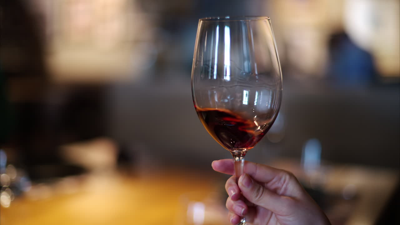 Primo piano di una donna che fa roteare del vino rosso in un bicchiere al ristorante