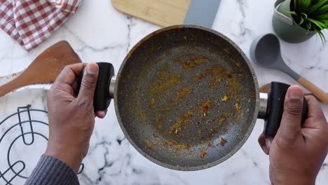 close up of hands holding a dirty pan with food scraps inside