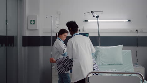 physician doctors helping patient to stand up from bed holding intravenous iv fluid drip bag