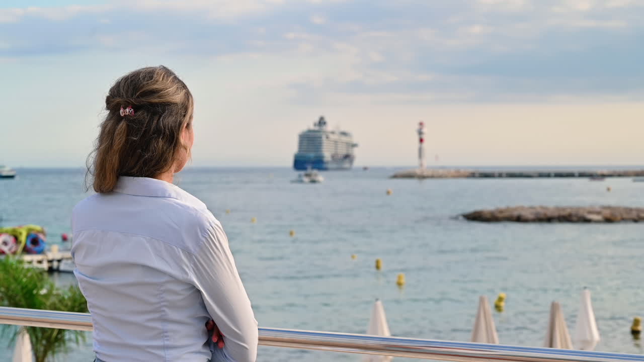 Rear view of a woman watching at the Mediterranean sea coast with ships and lighthouse in Cannes, France