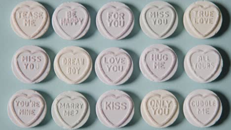 full frame shot of person choosing from heart candy with romantic messages of love on blue background