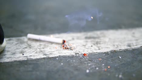 close up view of a cigarette falling down to the floor and being smashed by the male foot in the sneaker