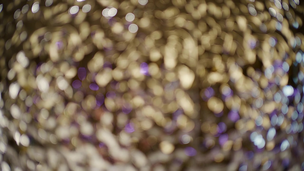 Abstract close up of golden, white, and purple bokeh lights with a soft glittering texture