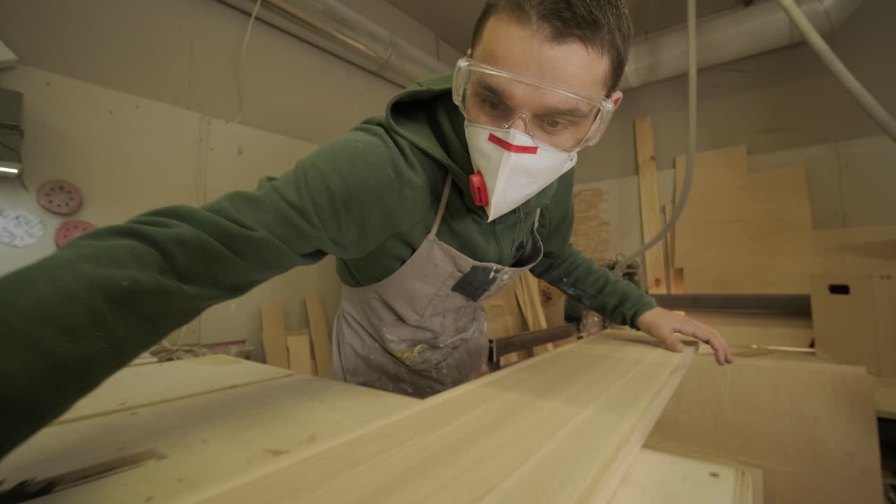 trabajador de la madera profesional en máscara y gafas comprueba la madera en bruto, tabla de madera, panel de contrachapado