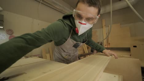 woodworker professional in mask and glasses checks wood raw, wooden plank, plywood panel