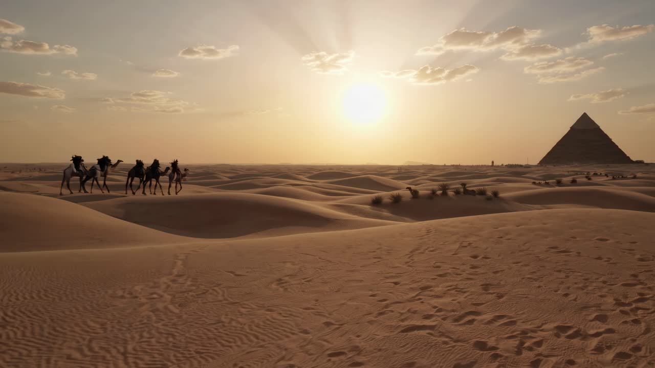Un video grandangolare cattura una carovana di cammelli che attraversa le dune del deserto al tramonto, con una piramide