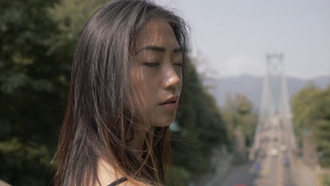 closeup of asian woman in black looking forward, lions gate bridge in background, slowmo