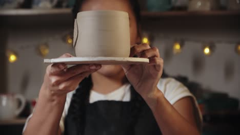 young woman potter looking at the final clay cup in her hands