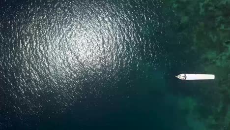 birds eye view of long boat resting on the turquoise indonesian shore - aerial top view fly-over