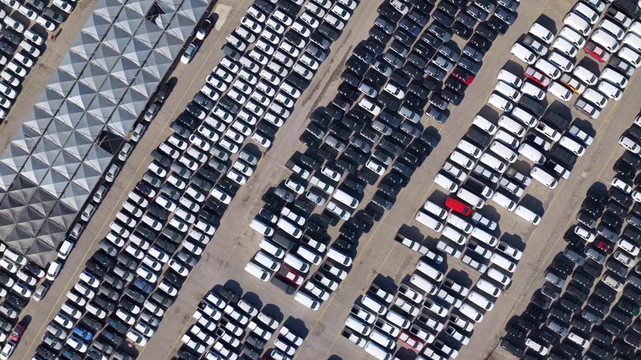 Bir otomotiv tesisinde düzenli sıralar halinde park edilmiş, sevkiyata hazır binlerce yeni arabanın kuşbakışı havadan görünümü — endüstride seri üretim, lojistik ve dağıtım.