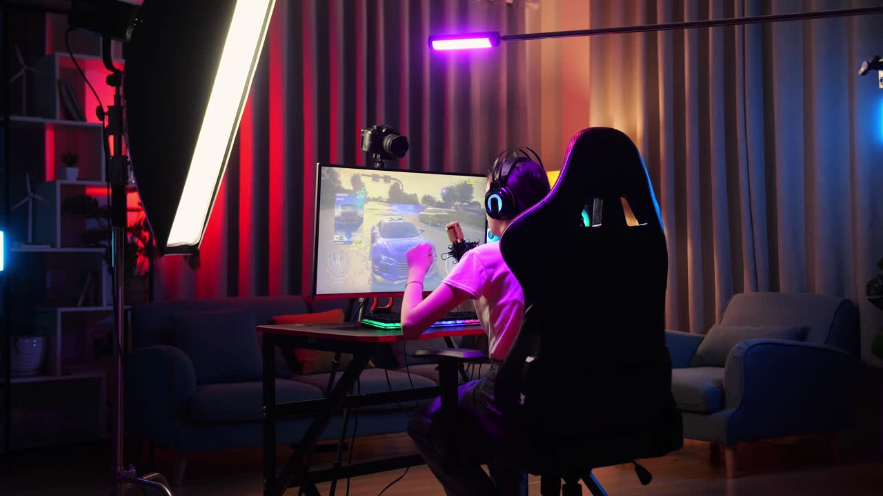 vista trasera de una chica asiática que juega a un juego de carreras de coches a través de la red en una computadora personal. bostezando y durmiendo, videojuego de transmisión en vivo, escritorio iluminado por luz de tira led rgb