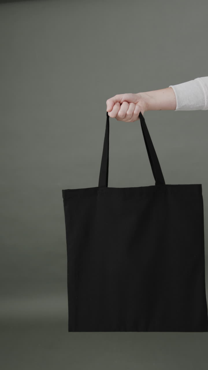 Vertical video of hand of caucasian woman with black canvas bag and copy space on grey background