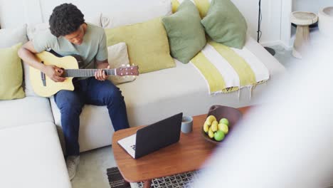 African-american-man-plays-guitar-and-singing,-using-laptop-at-home