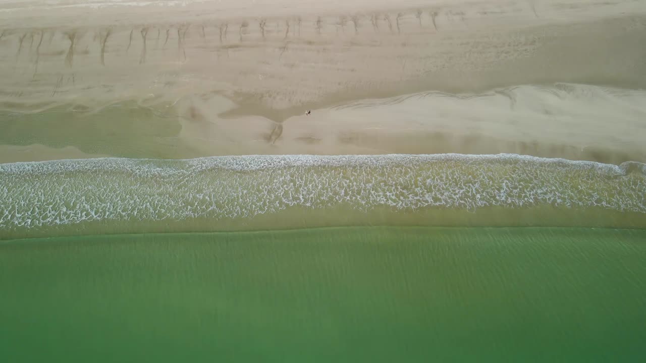 사람이 해변을 따라 걸을 때 파도가 침착하게 해변으로 부서집니다.