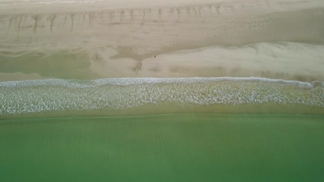 Waves-calmly-breaking-ashore-as-person-walks-along-beach