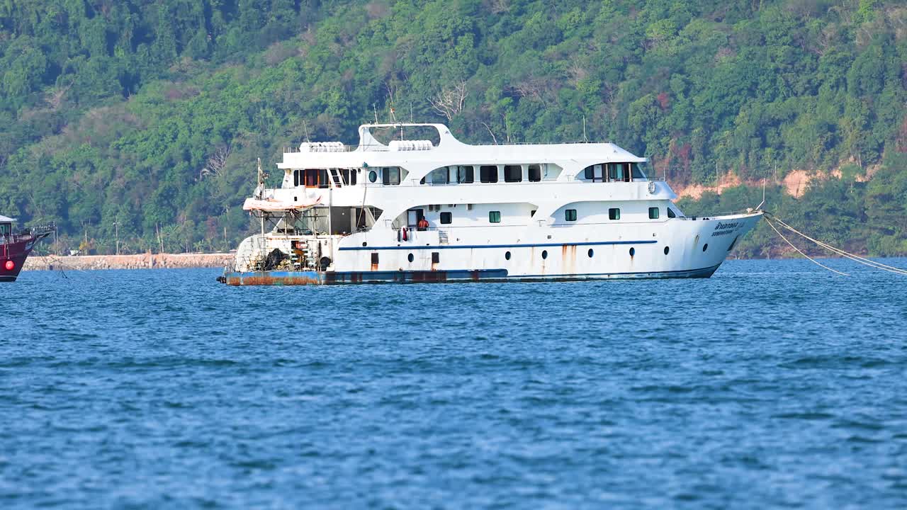 푸켓의 해안선을 따라 큰 색 요트가 항해하고 있습니다. 은 낮빛 아래 푸른 언덕을 배경으로