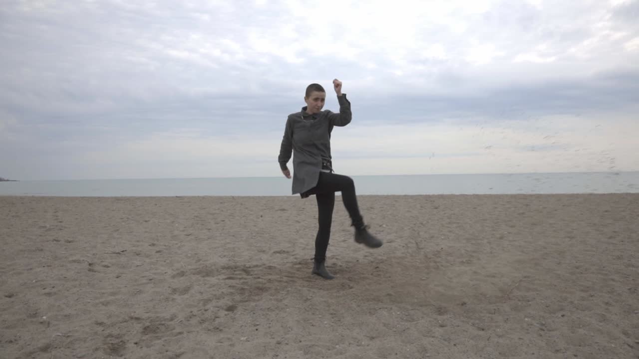 A Man Jump And Kicks The Sand Against The Clear Sky.- medium shot