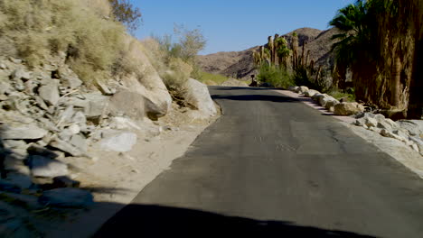 driving through “the rock drive-thru” at indian canyon in palm springs, california, surrounded by towering rock walls and desert landscape, under bright sunshine and a clear blue sky