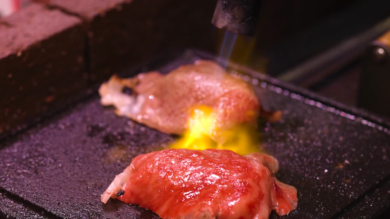 Detailed view of meat pieces being seared with a torch on a hot grill surface.