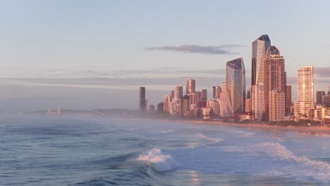 drone footage captures gold coast's skyline and ocean waves at sunrise, highlighting urban architecture and natural beauty