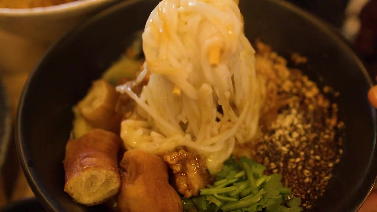 Le bacchette sollevano e mescolano noodles di tofu birmani caldi con curry di carne in una ciotola