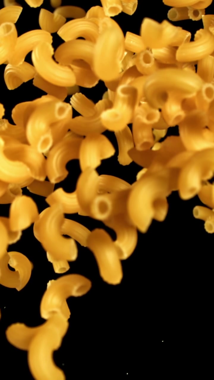Pasta maccheroni secca che cade al rallentatore su sfondo nero.