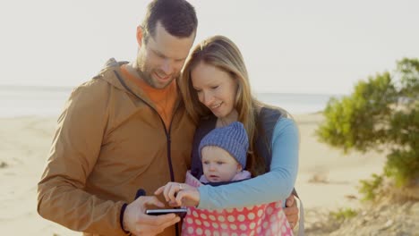 Vorderansicht-Einer-Kaukasischen-Familie,-Die-An-Einem-Sonnigen-Tag-Am-Strand-Ihr-Mobiltelefon-Benutzt,-4K