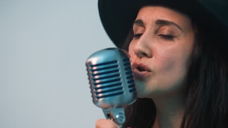 cantante femminile appassionata con cappello nero e giacca di pelle che si esibisce intensamente in un microfono vintage, con uno sfondo bianco morbido