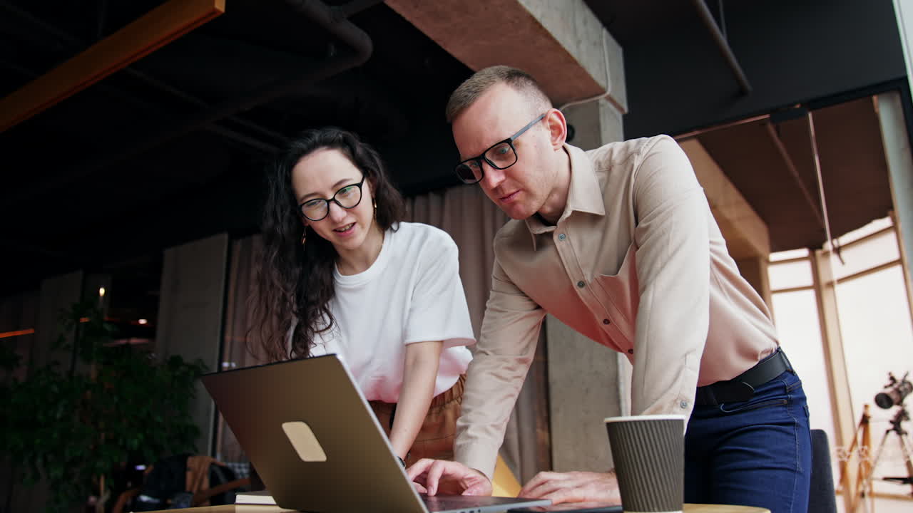 Coworkers stand bent over the laptop discussing the problem. Work on a project in the office. Low angle view.