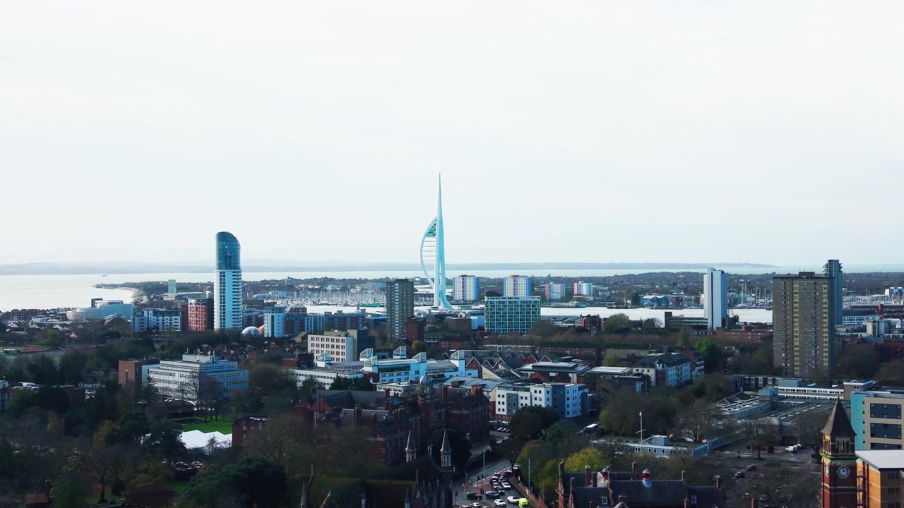 Riprese aeree con drone dello skyline di Portsmouth di giorno con la Spinnaker Tower, le acque del porto, un ponte distante e i tetti della città