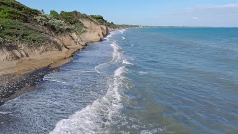 Vuelo-Aéreo-Hacia-Adelante-Sobre-Una-Playa-De-Guijarros-Y-Alcanzando-Olas-De-Mar-En-Verano---Bani,-República-Dominicana