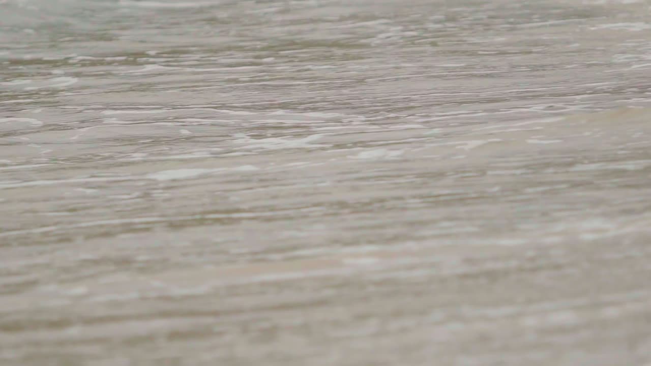 A powerful wave crashes onto the sandy beach at Sungai Pinang, West Sumatra, before receding back into the ocean. Captures the dynamic beauty of Indonesia's coastline.