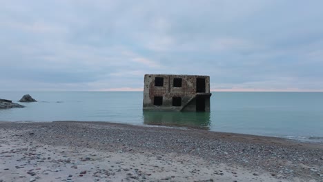 aerial view of abandoned seaside fortification building at karosta northern forts on the beach of baltic sea , waves splash, overcast day, wide drone shot rotate left