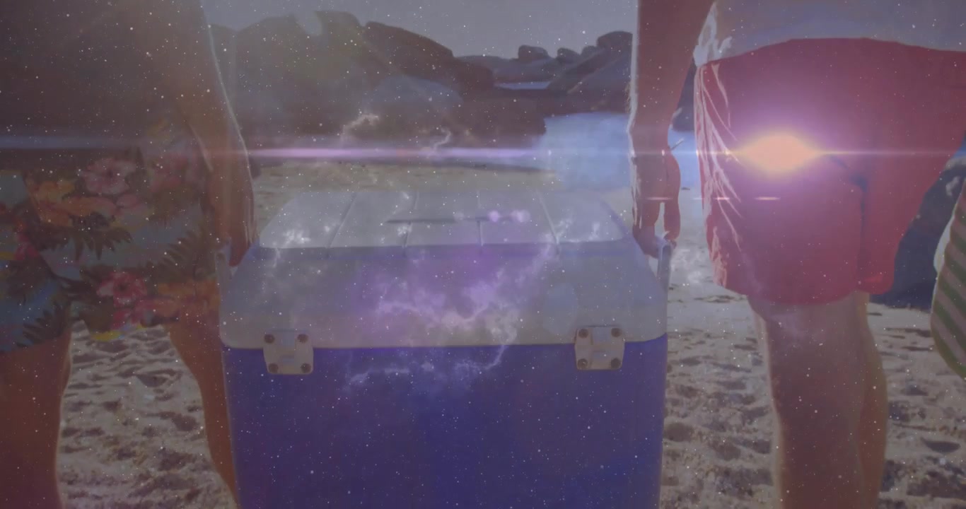 Dos hombres levantando las asas de una nevera portátil, caminando por una playa de arena hacia el agua con un cielo estrellado brillando para un viaje.