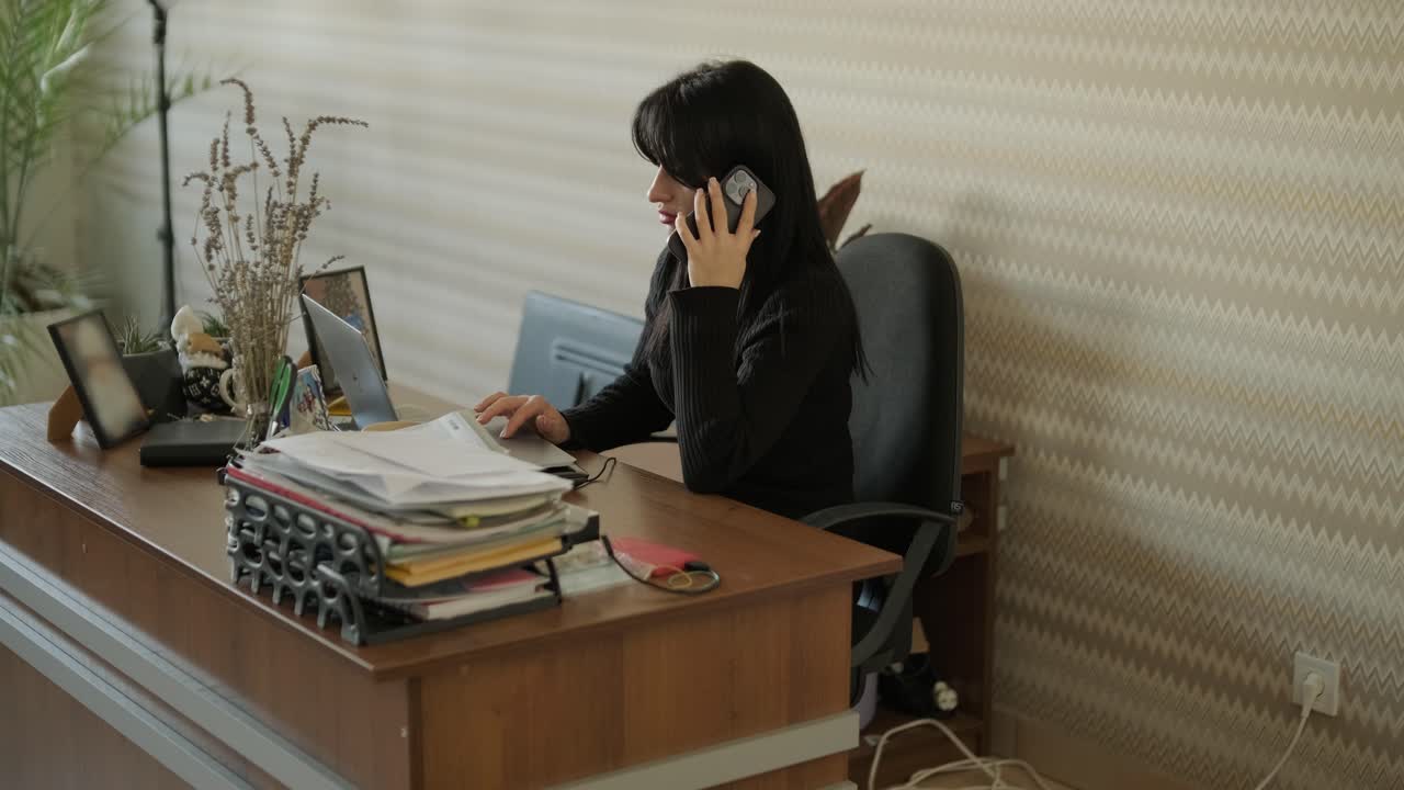 Donna professionista in un moderno ambiente d'ufficio, concentrata sul lavoro, vestita elegantemente in abiti da lavoro, circondata da attrezzature d'ufficio e un interno raffinato