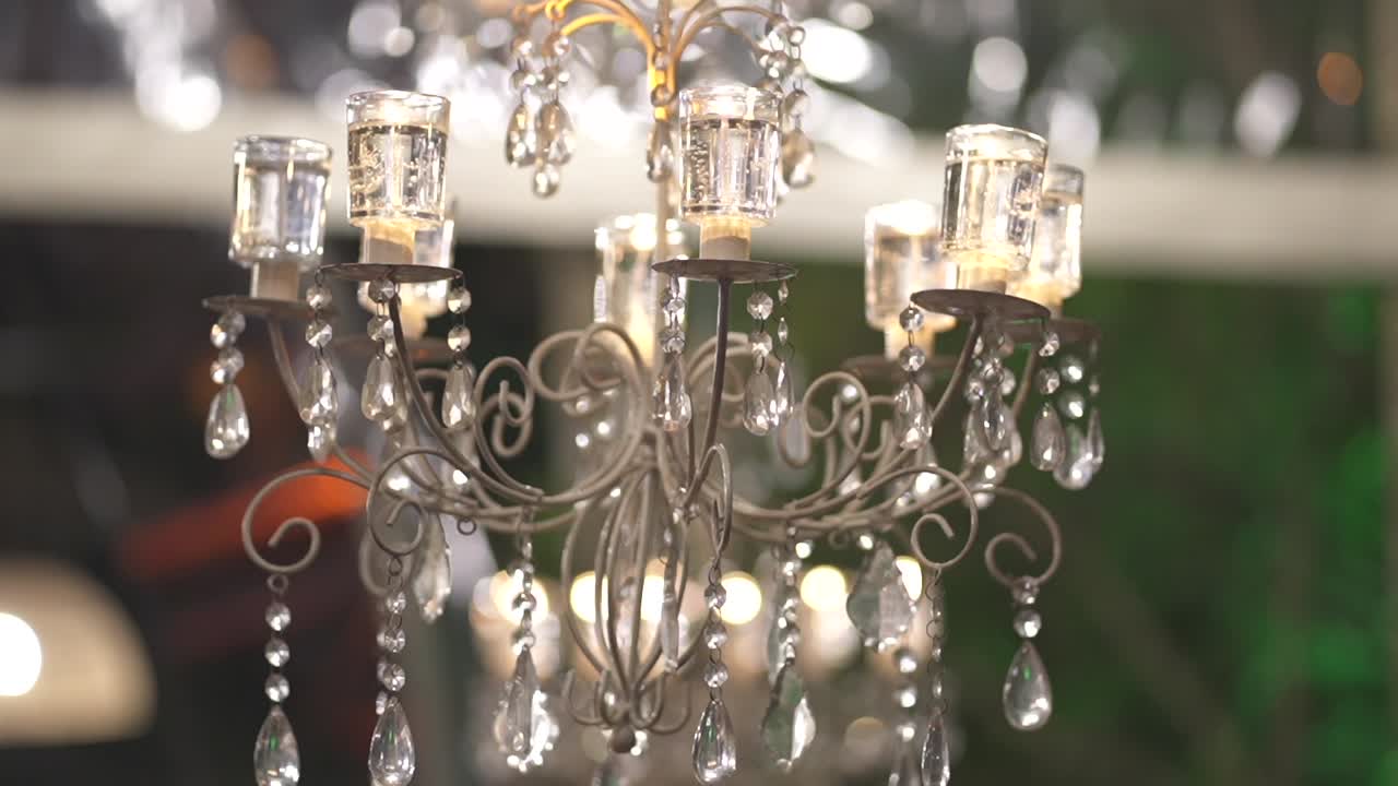 Close-up of a crystal chandelier illuminated warmly, with hanging glass prisms and graceful metal arms, showcasing sophisticated ambiance and luxurious details of wedding celebration, static camera