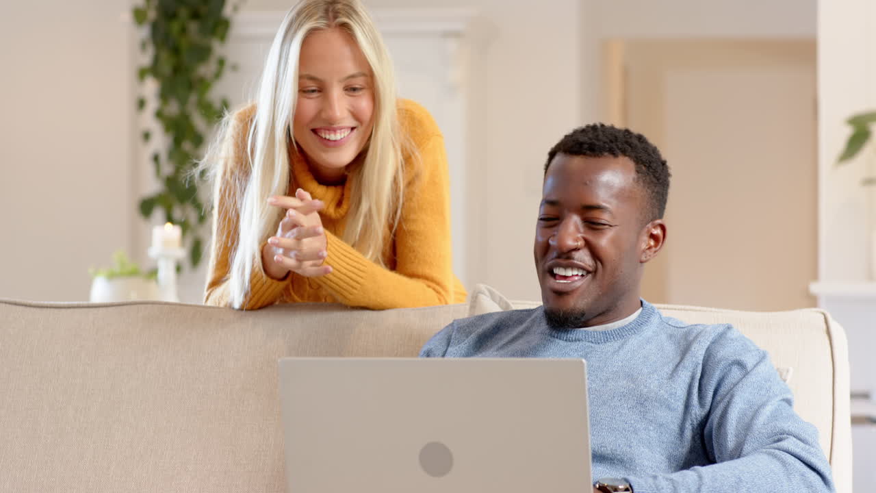 diverse couple enjoying cozy conversation at home with laptop, sharing joyful moments