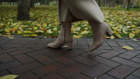 Cierra-Las-Piernas-De-Una-Mujer-Con-Botas-Caminando-Por-La-Pasarela-Del-Parque.-Zapatos-Yendo-Lentamente