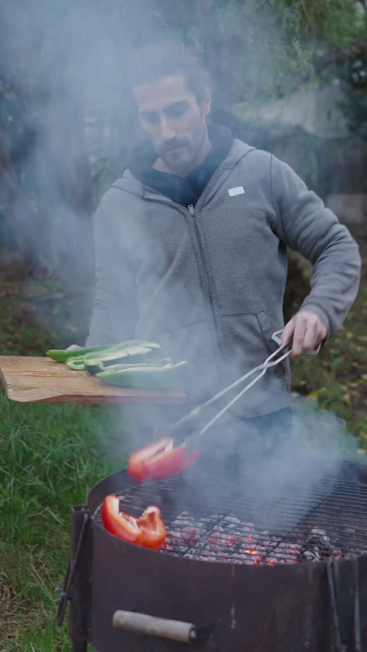 Man grilling peppers outdoors on a charcoal barbecue