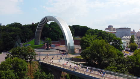 Drone-slowly-ascending-to-reveal-a-huge-rainbow-shaped-arch-monument-near-pedestrian-bridge-in-a-capital-of-Ukraine