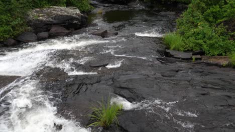 Felsiger-Fluss,-Der-Stromabwärts-Plätschert---Wildwasserbach-über-Schwarzen-Felsen,-Umgeben-Von-Grüner-Vegetation