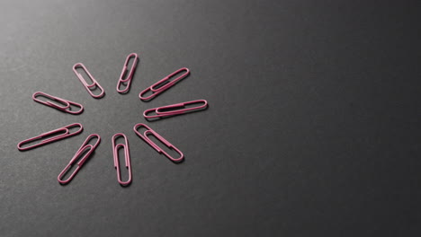 primer plano de clips de papel rosados dispuestos con espacio de copia en fondo negro, en cámara lenta