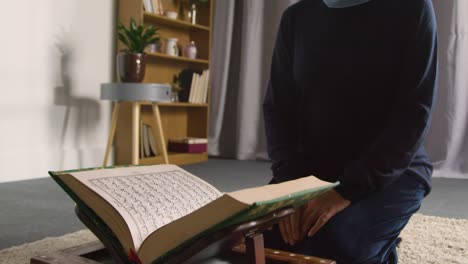 close up of muslim woman at home kneeling and reciting from the quran 3