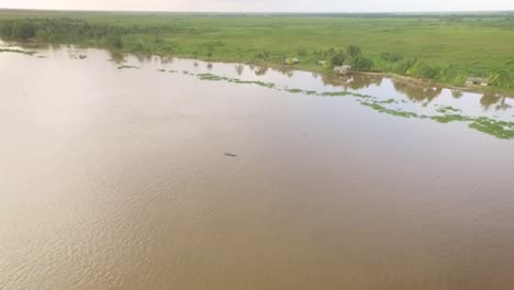 vista aérea de una pequeña canoa indígena flotando en el río orinoco con pequeñas casas indígenas en la orilla