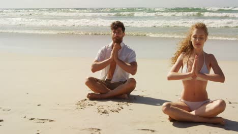 Couple-performing-yoga-at-beach-on-a-sunny-day-4k