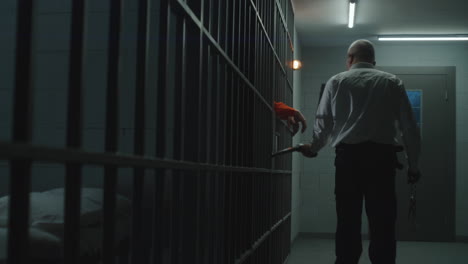 prison employee with police baton watches criminals in prison cells