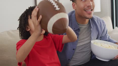 happy biracial man and his son watching american football match together