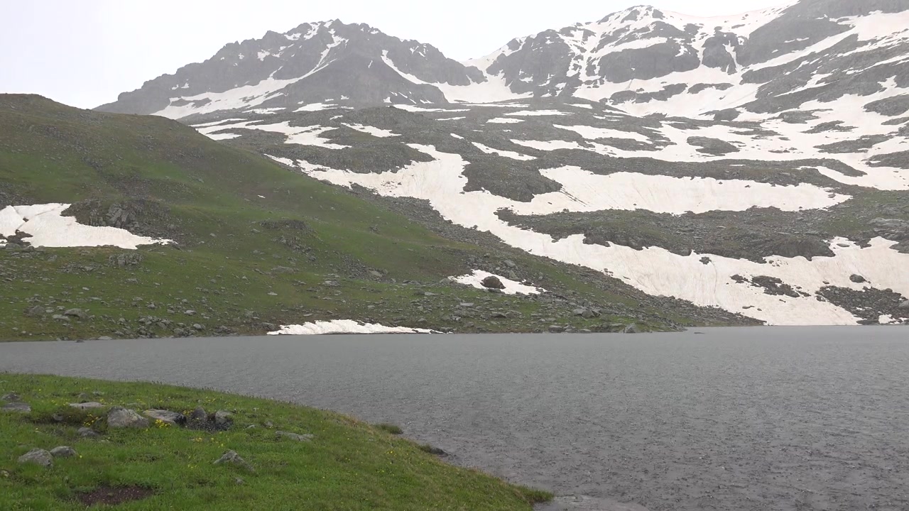 Regn faller på en høyfjellsinnsjø med snødekte fjell