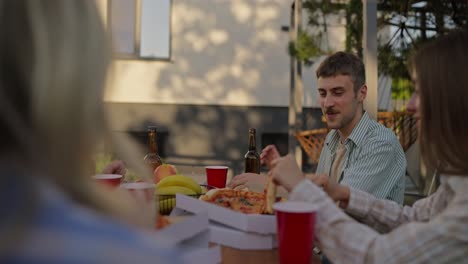 Happy-blond-guy-with-a-mustache-arranges-boxes-of-pizza-and-takes-a-slice-for-himself-during-a-shared-lunch-in-the-courtyard-of-a-country-house